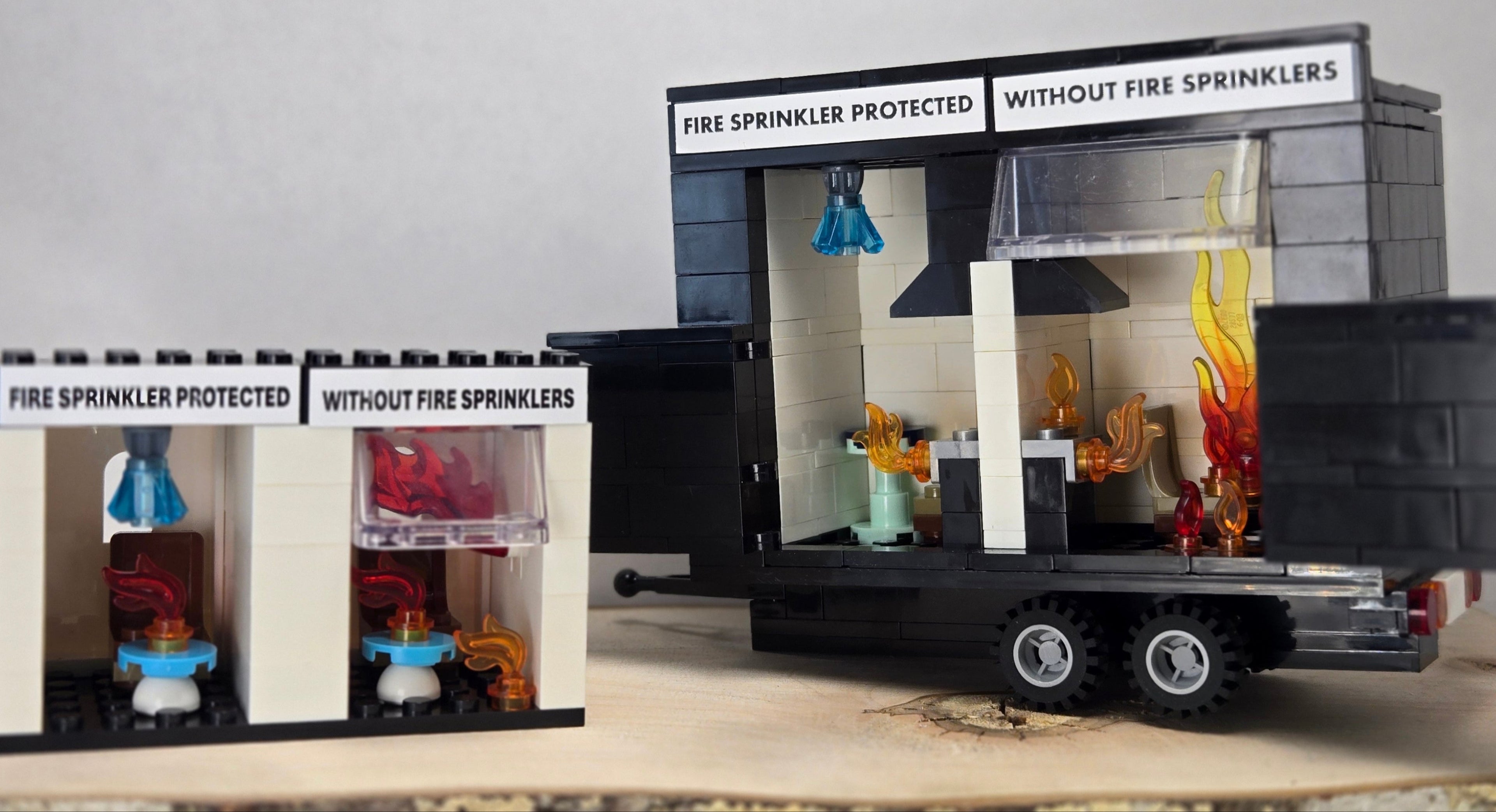 LEGO-compatible fire sprinkler demonstration kits showing two-sided scenes — one side labeled "Fire Sprinkler Protected" with custom sprinkler brick and blue crystal water spray, and the opposite side labeled "Without Fire Sprinklers" with flames representing flashover.