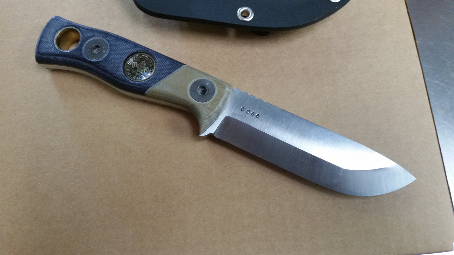 Custom knife made from O‑1 tool steel with handle crafted from Cub Scout uniform micarta, featuring inlaid button as bow‑drill hand socket for primitive fire making. Unique piece blending scouting heritage with functional survival design.