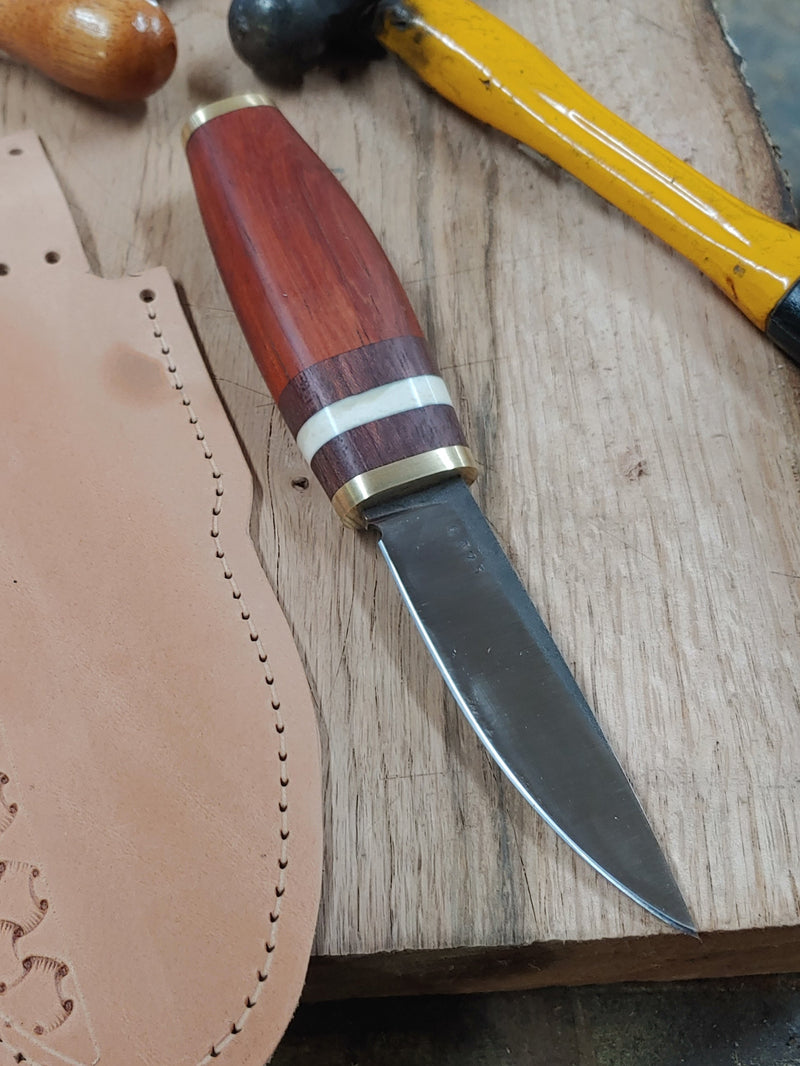 “Puukko‑style knife made as a thank‑you gift, featuring a 440C stainless steel blade, brass hilt and pommel, redheart and purpleheart wood handle with a white spacer, and a tooled leather sheath.