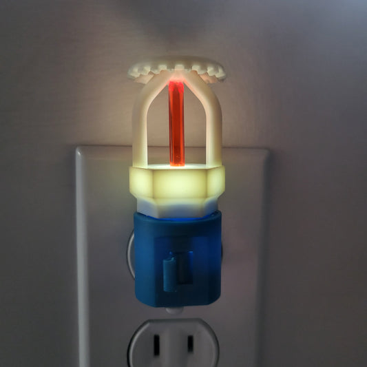 Straight‑on view of affordable fire sprinkler night light in blue base, red‑bulbed upright head softly glowing in dim room and casting subtle shadow on wall, designed for kids or families in the fire safety community.