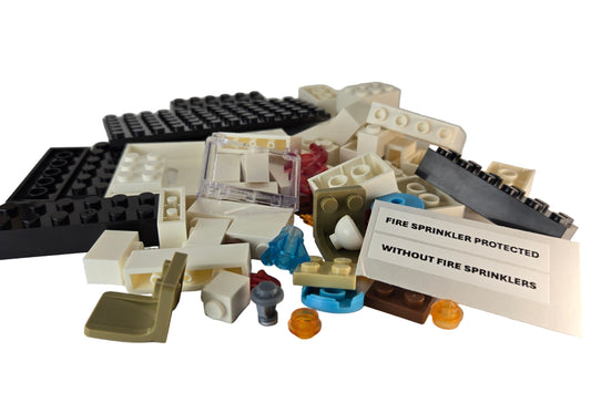 Unassembled mini fire sprinkler demo kit showing all building block pieces and sticker sheet labeled ‘Fire Sprinkler Protected’ and ‘Without Fire Sprinklers.