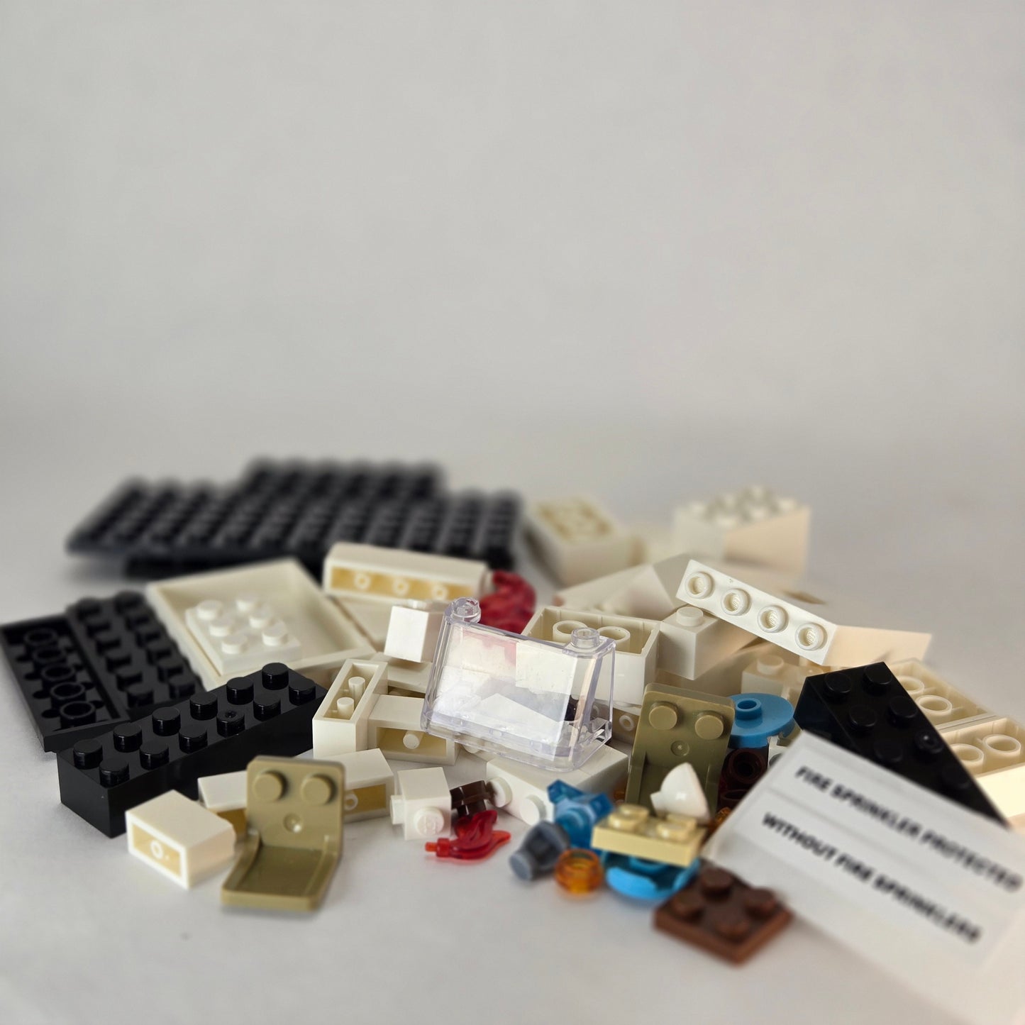 Unassembled mini fire sprinkler demo kit with all building block pieces, sticker sheet for ‘Fire Sprinkler Protected’ and ‘Without Fire Sprinklers,’ and the included clear windscreen accessory.