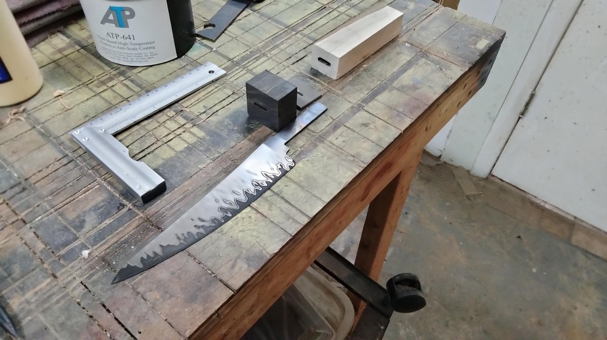 In‑progress image of hand‑forged San‑Mai blade before handle shaping, showing Gaboon ebony, silver maple, and stainless spacer components alongside patterned blade.