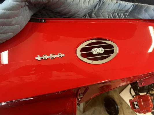 Shiny nickel‑plated MGA 1850 emblem installed on side vent of classic MGA during restoration, highlighting accurate fit and period‑correct style.