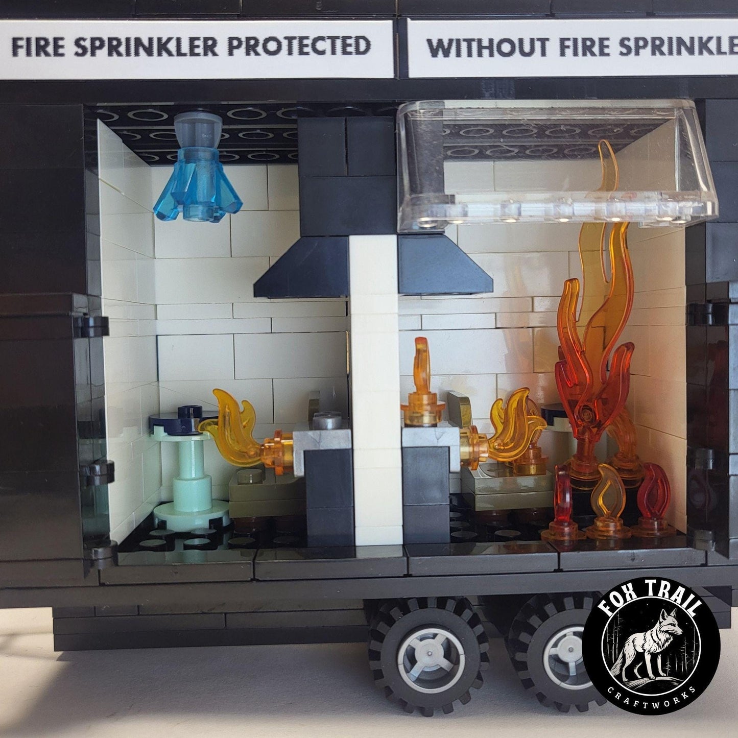 Close‑up of burn trailer interior showing detailed kitchen scenes; sprinkler‑protected side has blue water crystal activation, while the unprotected side is engulfed in flames to demonstrate flashover during fire safety education.