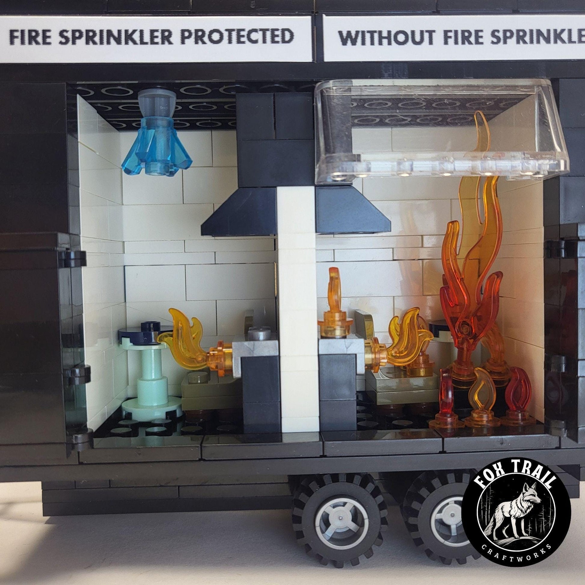Close‑up of burn trailer interior showing detailed kitchen scenes; sprinkler‑protected side has blue water crystal activation, while the unprotected side is engulfed in flames to demonstrate flashover during fire safety education.