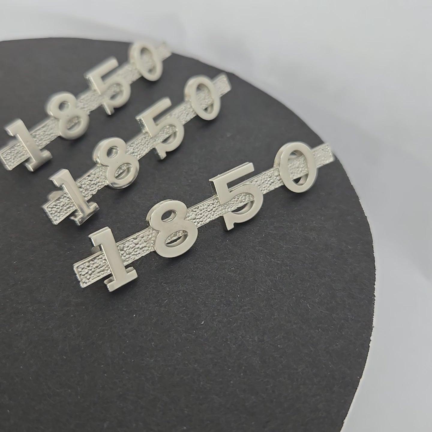 Rotating view of three MGA 1850 emblems, showcasing polished nickel finish, precise detailing, and subtle handmade variations for restorations.