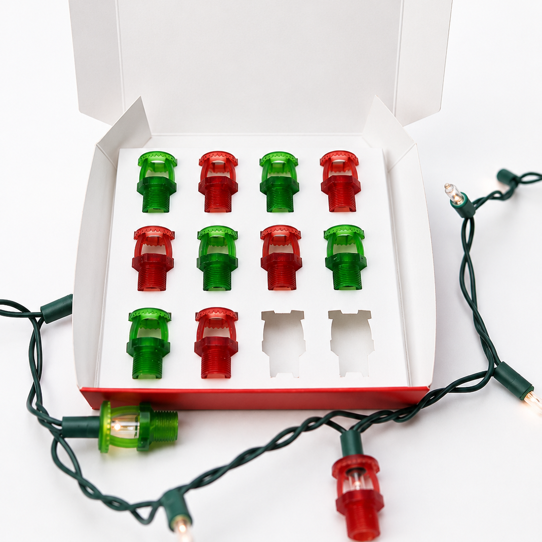 Set of red and green light bulb covers, shaped like fire sprinklers, in a box with Christmas lights on a white background