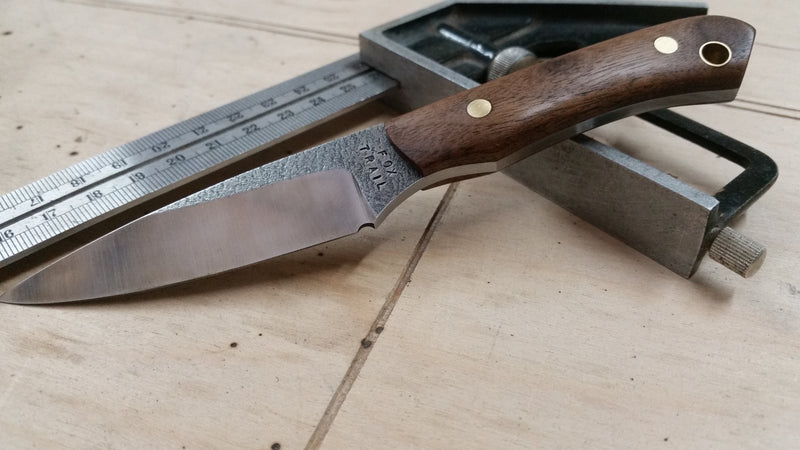 Neck knife with 440C stainless steel blade and walnut handle, rough‑finished blade flats, displayed on a carpenter’s square.
