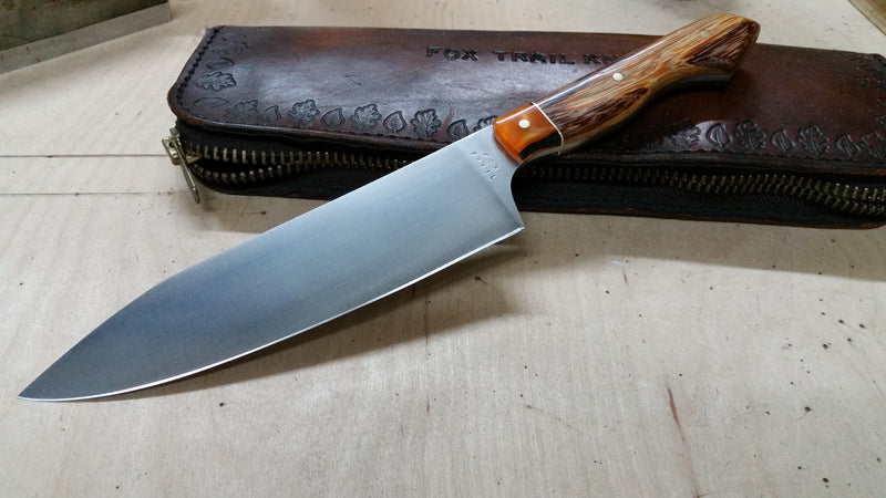 Chef’s knife with 1095 high carbon steel blade, acrylic bolsters with brass accents, and marble wood handle. Handmade by Fox Trail Craftworks, combining striking materials and functional design for culinary use or collectors of unique kitchen knives.