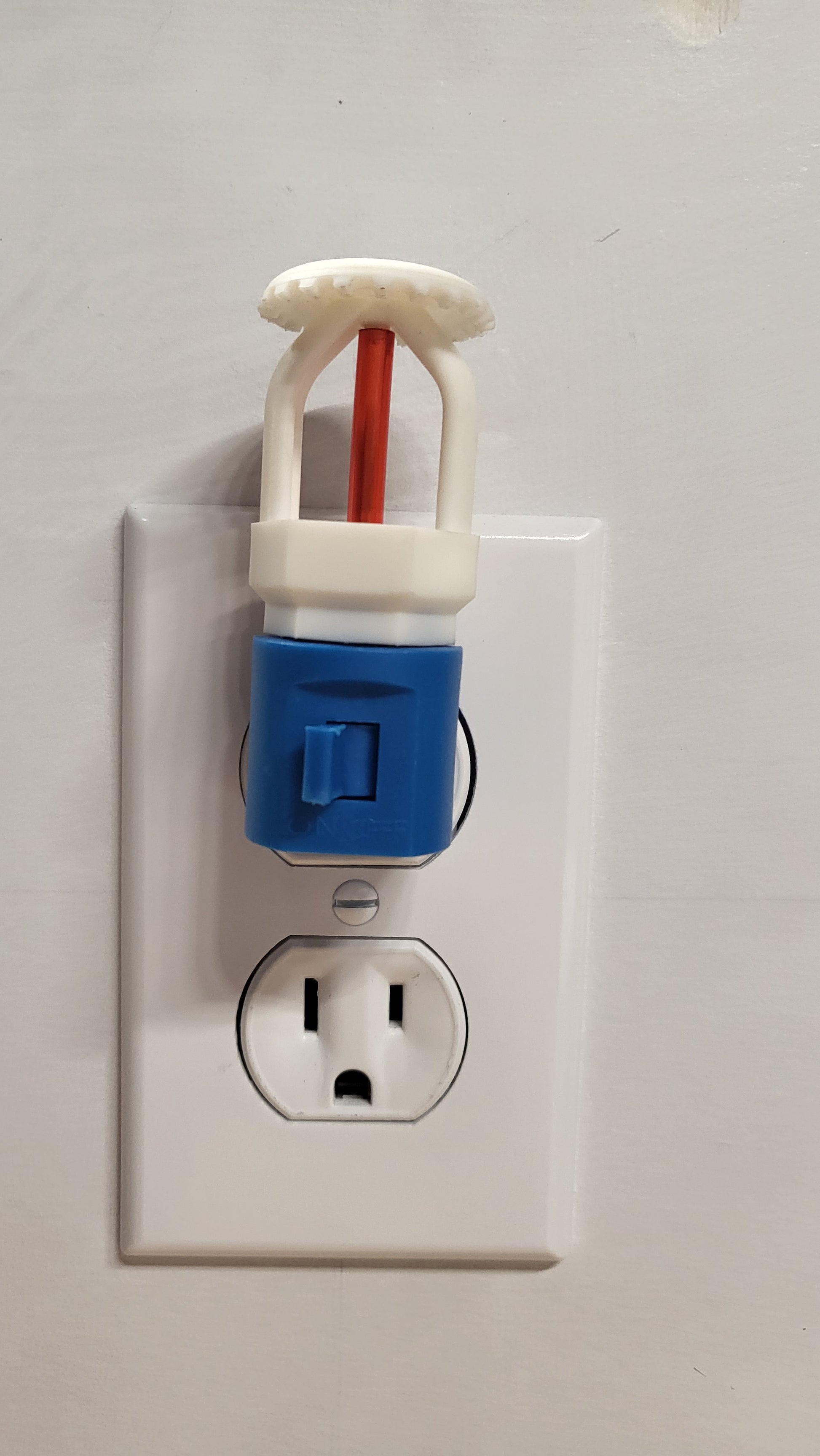 Straight‑on view of white upright fire sprinkler night light with red bulb on blue base with switch, plugged into wall outlet in off position against clean white wall.