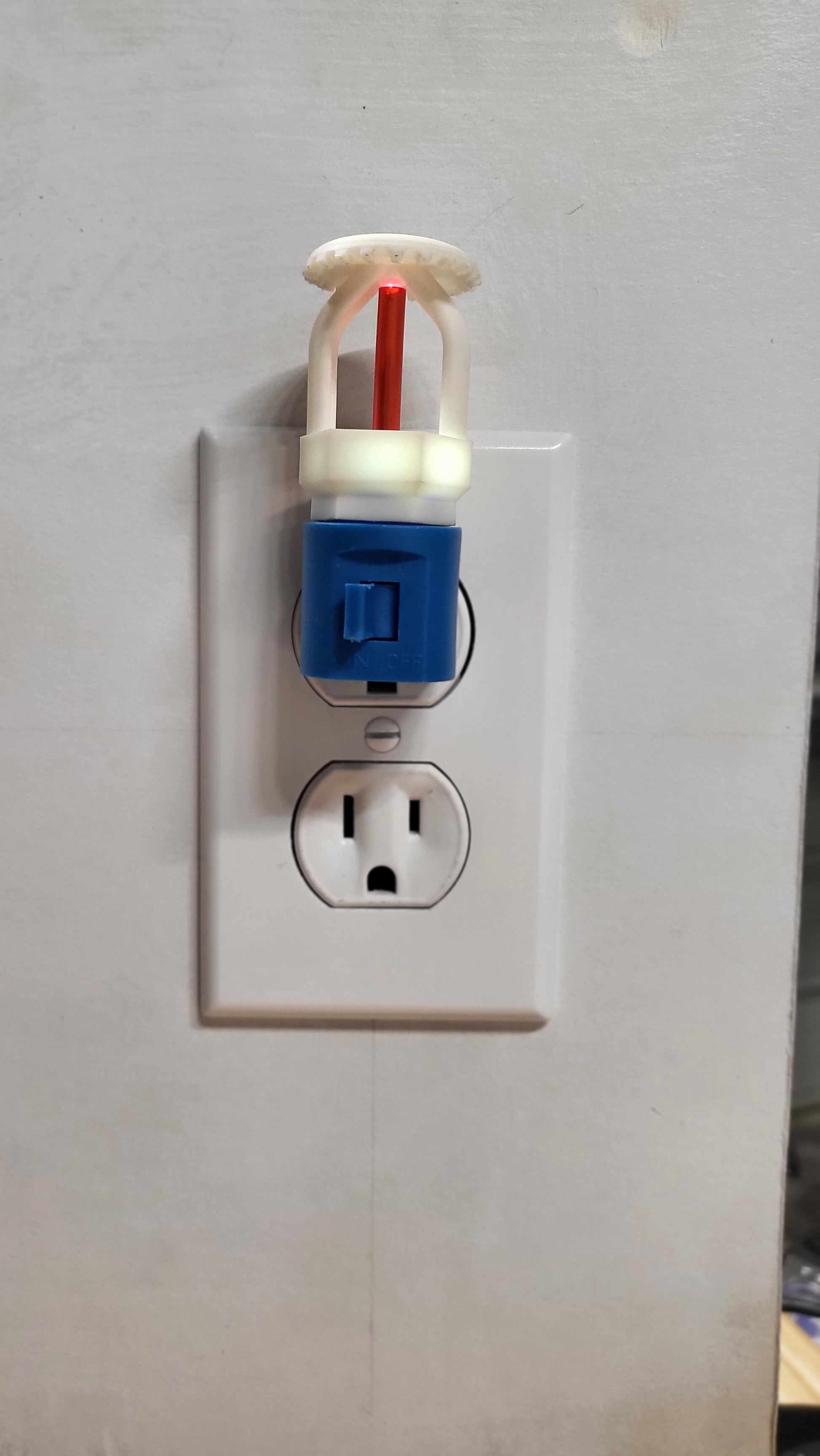 Straight‑on view of  fire sprinkler night light in blue base glowing faintly even in a lit room, white upright head with red bulb reflecting fire protection style for children’s bedrooms or family spaces.