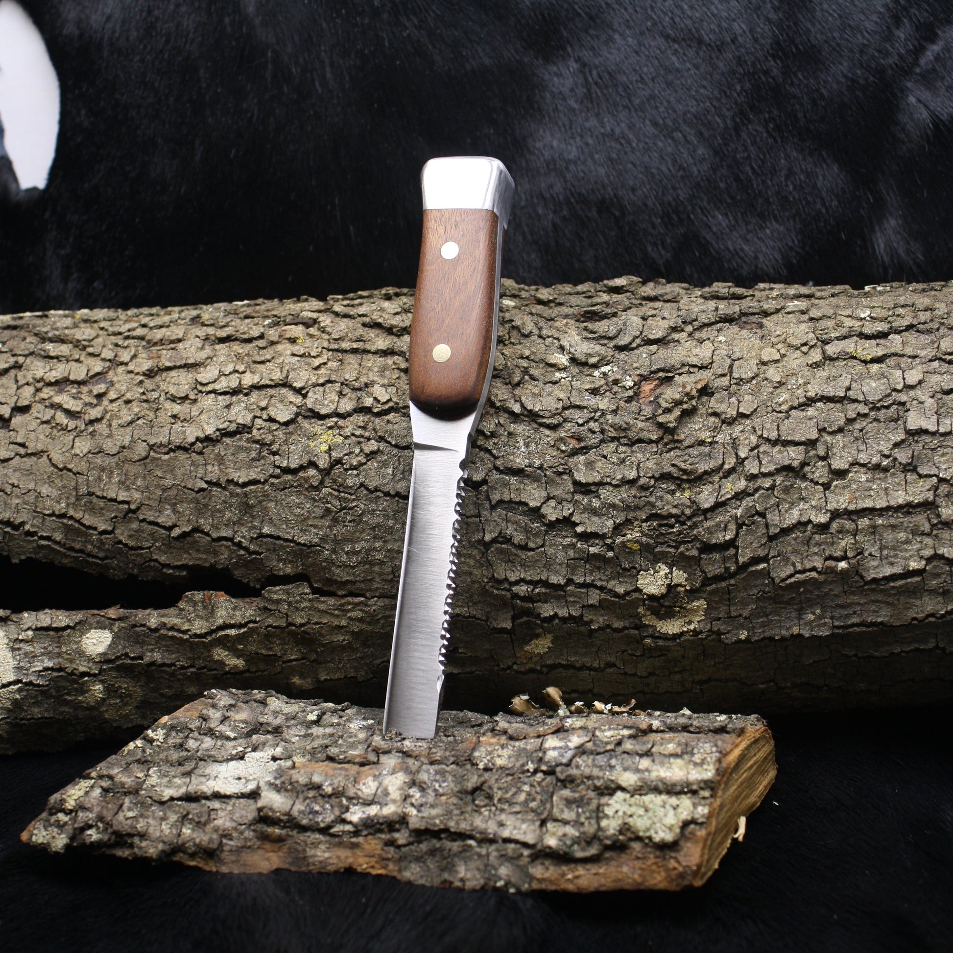 Knife with wooden handle on a log against a black background