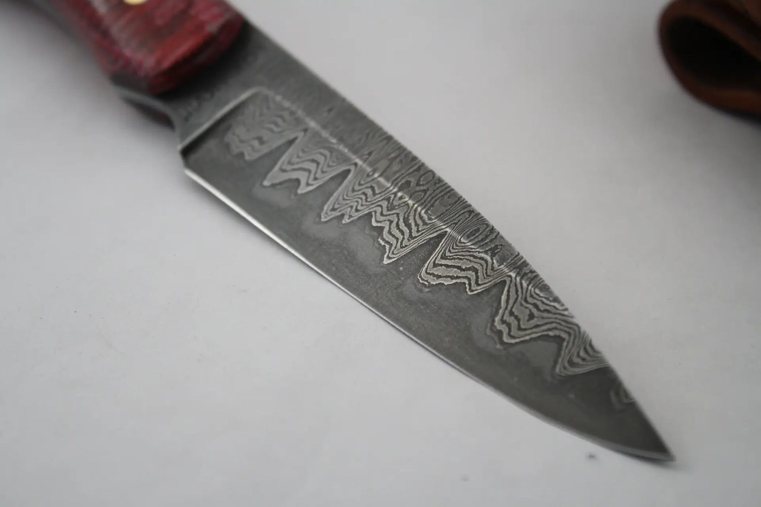 Close‑up of raindrop Damascus blade made from fire sprinkler pipe jacketed around 1095 steel, showing striking darkened edge contrast. Handle crafted from repurposed fire hose in micarta style, highlighting unique fire protection materials.