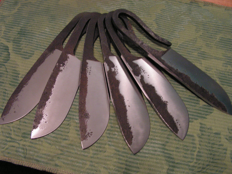 Set of six blacksmith‑style knives forged from 1095 steel with flat‑ground drop point blades and rough‑forged finish, made as groomsmen gifts.