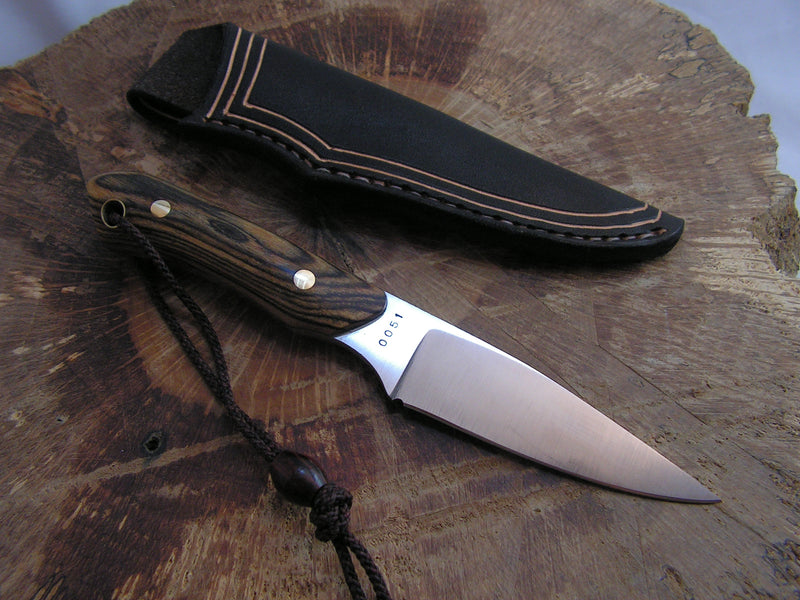 Stainless steel neck knife with a bocote wood handle, displayed on a wooden surface with a handmade leather sheath.