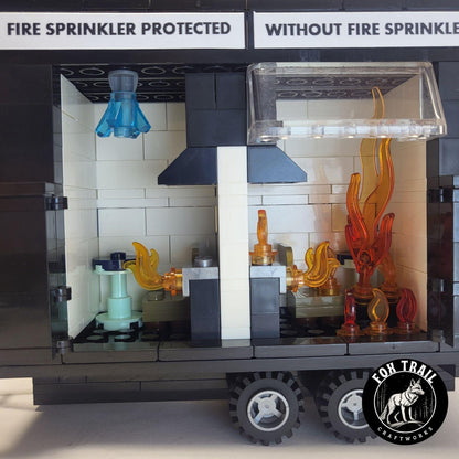 Close‑up of burn trailer interior showing detailed kitchen scenes; sprinkler‑protected side has blue water crystal activation, while the unprotected side is engulfed in flames to demonstrate flashover during fire safety education.